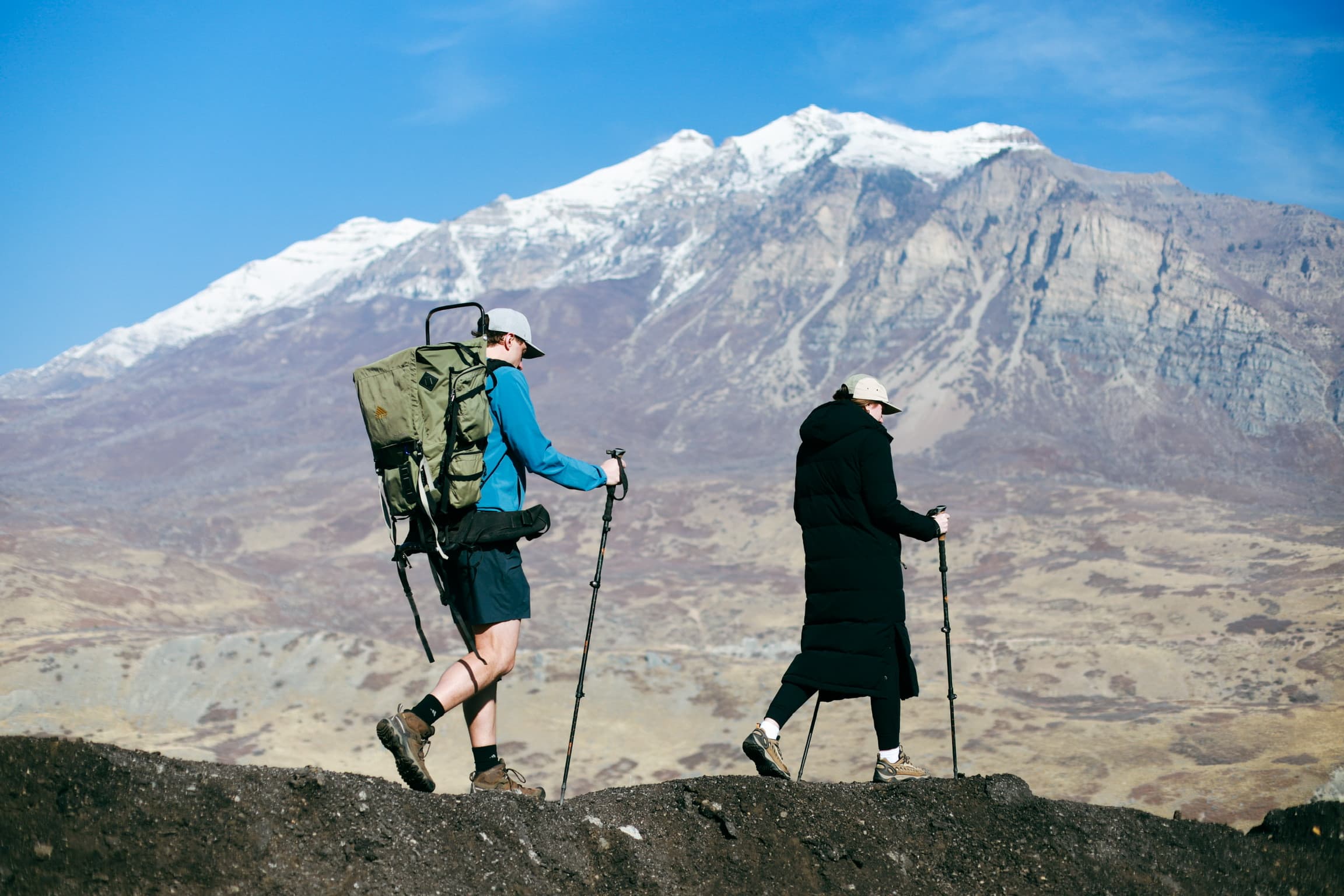 Two hikers with Kiba backpack against snow-capped mountain backdrop